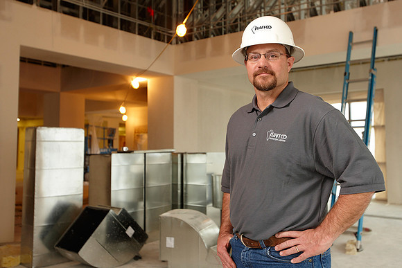 A Flintco Contruction employee posed proudly for his business portrait, with his hands on his hips in front of a home renovation site.