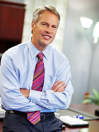 Executive headshot of a business man smiling casually at the camera in an office environment