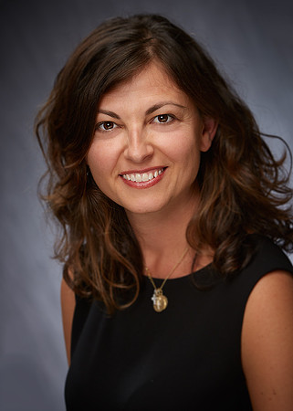 Professional business woman smiling at the camera on a grey neutral background. She looks relaxed and happy.