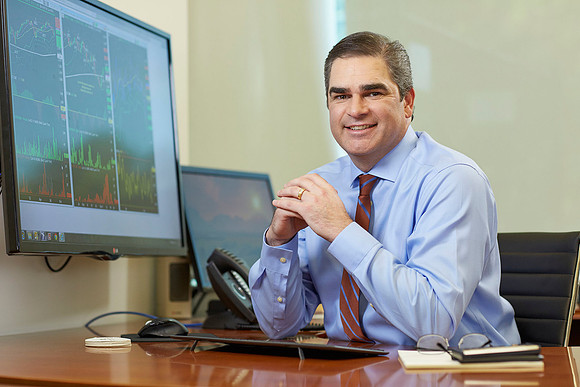 Professional Business Headshot of an executive male in an office environment smiling at the camera showing graphs on the computer.