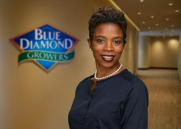 Simone-Denny-in-hallway-w-Blue-Diamond-Logo-Background-700x500px-Saved4WEB-